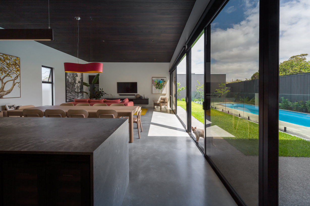 Luxury dining area and modern kitchen with timber finishes, large island bench and floor-to-ceiling glazing